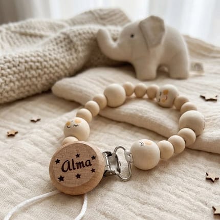 Personalizēts koka knupīšu turētājs ar bērna vārdu un emociju bumbiņām. Pieejamas diega krāsas – sarkana, zaļa, balta. Roku darbs un ideāla dāvana mazulim!
